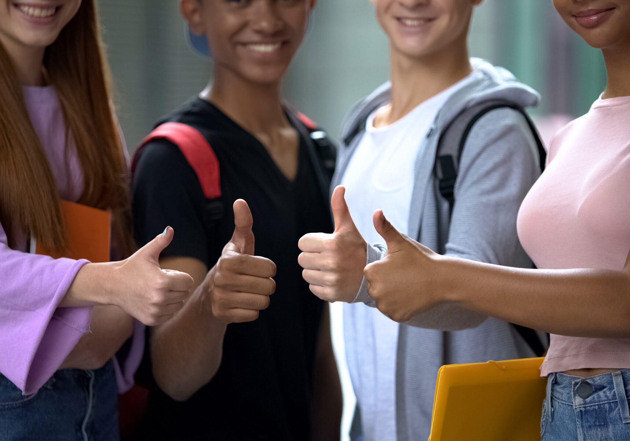 Happy mixed-race friends with books showing thumbs up, student exchange program